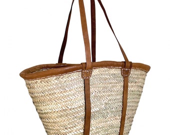 May include: Woven straw tote bag with brown leather trim and handles. The bag features a natural straw color with a brown leather rim and straps, and white stitching details. The bag is designed for carrying items.