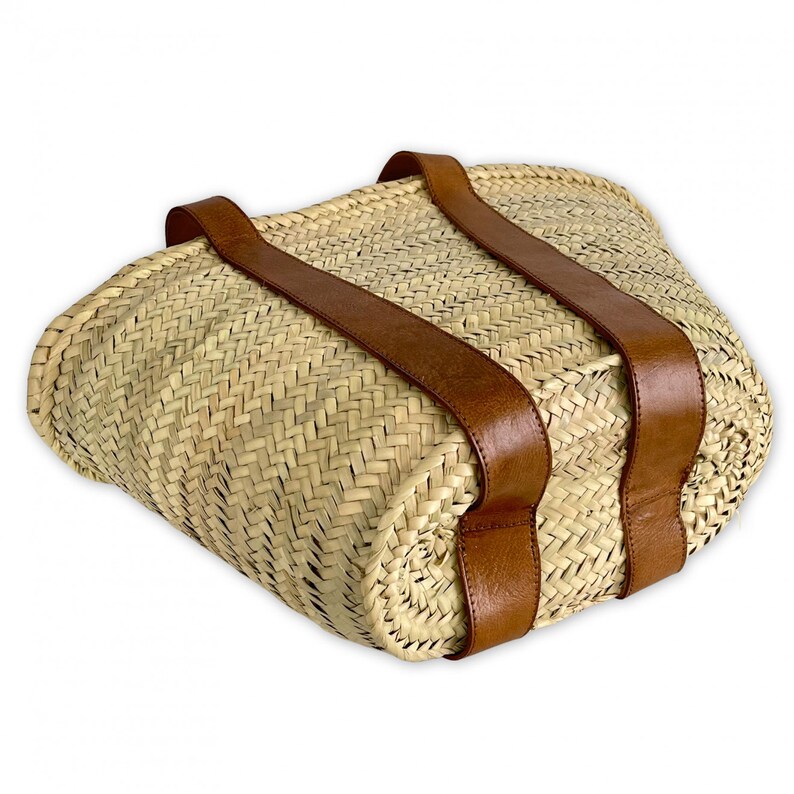 May include: A woven straw tote bag with brown leather straps. The bag has a rounded shape and a woven pattern.