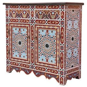 Op de afbeelding: Een decoratieve kast met een donkerbruin bovenblad en ingewikkelde geometrische patronen. De kast heeft een rode achtergrond met blauwe, witte en gouden accenten. De deuren en zijkanten zijn versierd met stervormige ontwerpen en bloemmotieven.