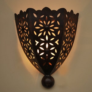 Op de afbeelding: Een zwarte metalen wandlamp met een decoratief uitgesneden ontwerp. De lamp heeft een ronde gloeilamp in het midden en een decoratief eindstuk aan de onderkant.