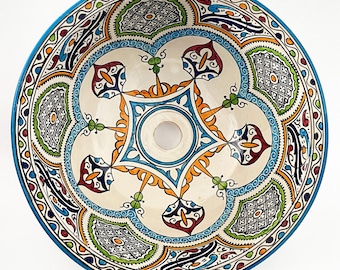 May include: A white ceramic sink with a blue rim and intricate colorful Moroccan-style designs. The sink has a round shape and a central drain hole.