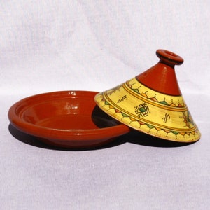 May include: A traditional Moroccan tagine cooking pot with a red clay base and a yellow and orange cone-shaped lid with geometric designs.
