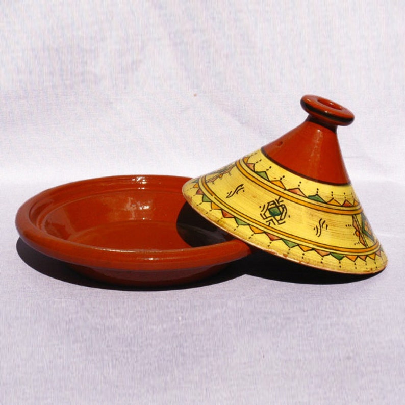 May include: A traditional Moroccan tagine cooking pot with a red clay base and a yellow and orange cone-shaped lid with geometric designs.
