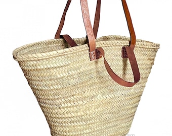 May include: A large, woven straw tote bag with brown leather handles. The bag is made of a natural, light brown straw and has a wide, open top.