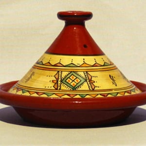 May include: A red ceramic tagine with a yellow and green geometric design. The tagine is a traditional Moroccan cooking pot with a conical lid.
