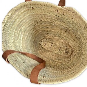 May include: A large, woven straw tote bag with brown leather handles. The bag is empty and the inside is visible.