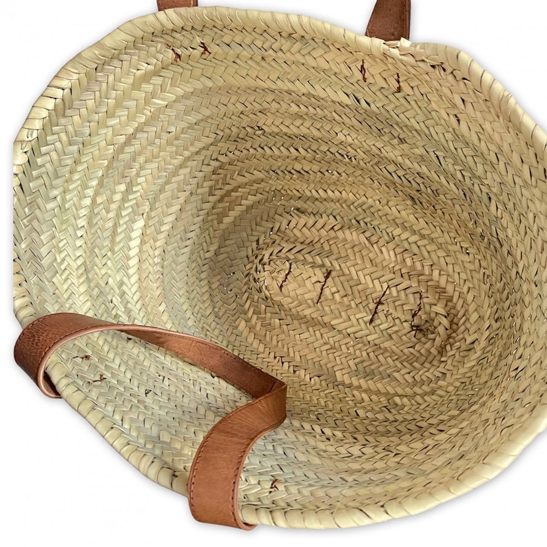 May include: A large, woven straw tote bag with brown leather handles. The bag is empty and the inside is visible.