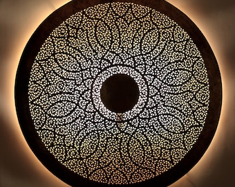 May include: A round, metal ceiling light fixture with a intricate, cut-out design. The light fixture is illuminated from behind, creating a warm glow.