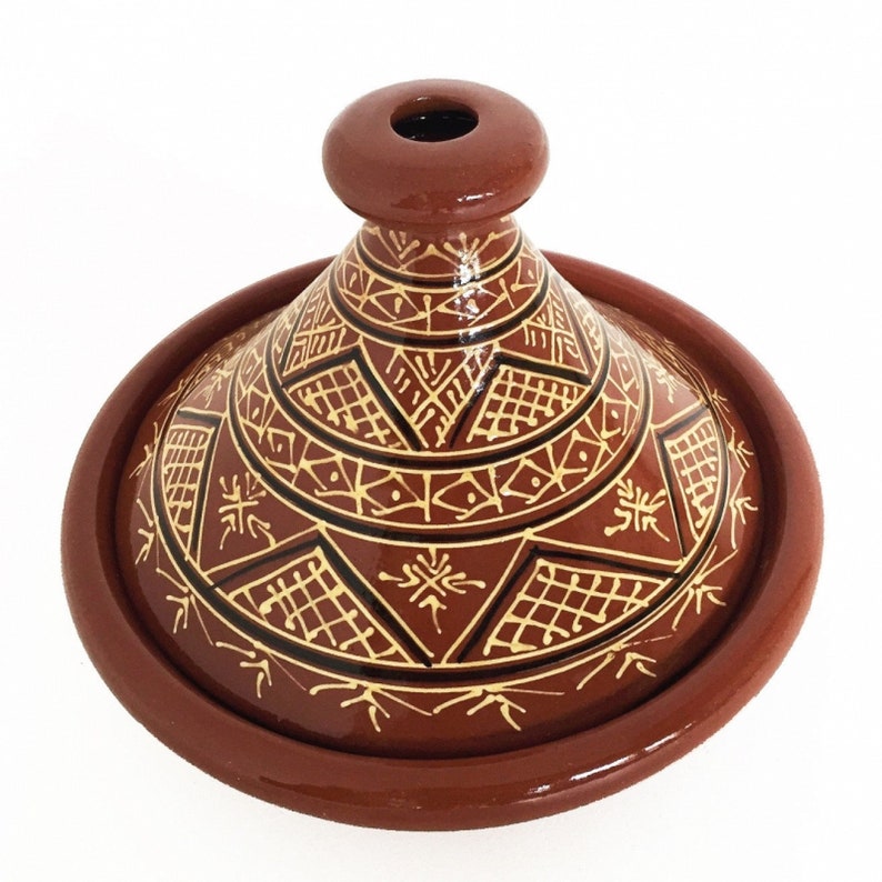 May include: A terracotta tagine with a conical lid featuring intricate geometric patterns in gold and black. The tagine is a traditional Moroccan cooking pot.