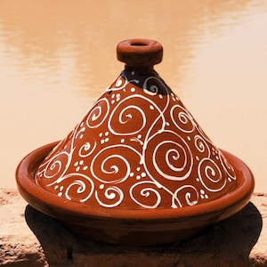 May include: A terracotta tagine with a white swirl design. The tagine has a round base and a conical lid with a small knob on top.