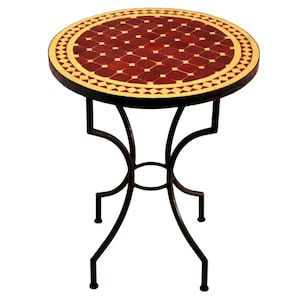 Op de afbeelding: Een ronde bijzettafel met een mozaïektegelblad. Het tafelblad heeft een patroon van rode en crèmekleurige tegels. De donkerbruine metalen basis heeft een decoratief, gebogen ontwerp. De tafel is geschikt voor binnen of buiten.
