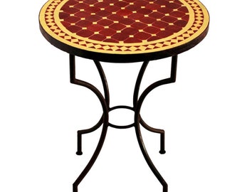 May include: A round side table with a mosaic tile top. The tabletop features a pattern of red and cream-colored tiles. The dark brown metal base has a decorative, curved design. The table is suitable for indoor or outdoor use.