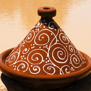 Könnte beinhalten: Eine Terrakotta-Tajine mit einem weißen Wirbelmuster. Die Tajine ist ein traditioneller marokkanischer Kochtopf mit einem konischen Deckel.