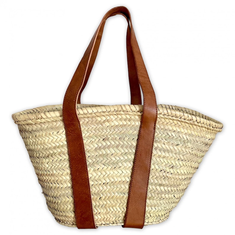 May include: A large, woven straw tote bag with brown leather handles. The bag is made of a natural, light brown straw and has a wide, open top.