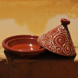 May include: A terracotta tagine with a white swirl design. The tagine is a traditional Moroccan cooking pot with a conical lid.