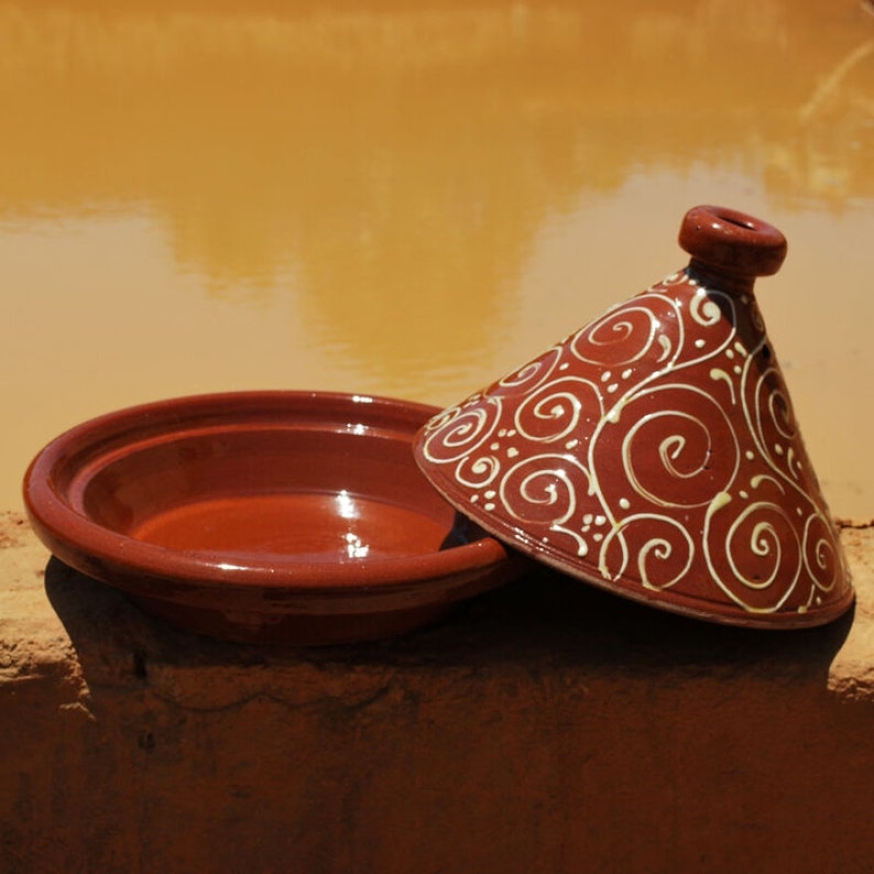 May include: A terracotta tagine with a white swirl design. The tagine is a traditional Moroccan cooking pot with a conical lid.