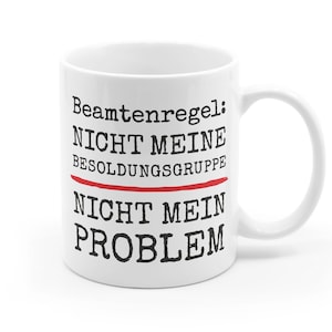May include: White ceramic mug with black text that reads "Beamtenregel: Nicht meine Besoldungsgruppe Nicht mein Problem". The text "Besoldungsgruppe" is underlined in red.