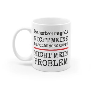 May include: White ceramic mug with black text that reads "Beamtenregel: Nicht meine Besoldungsgruppe Nicht mein Problem". The word "Besoldungsgruppe" is underlined in red.