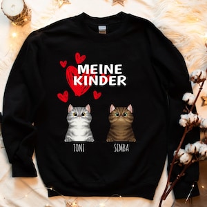 Könnte beinhalten: Schwarzer Pullover mit dem Text "Meine Kinder" in weißen Buchstaben und zwei Comic-Katzen mit den Namen "Toni" und "Simba" darunter. Der Text ist von roten Herzen umgeben.