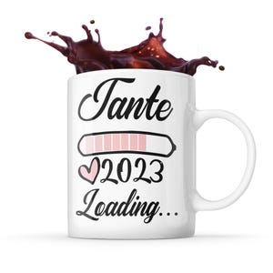 Könnte beinhalten: Weiße Keramiktasse mit einem schwarzen und rosafarbenen Design. Die Tasse trägt den Text "Tante 2023 Loading..." mit einem rosafarbenen Fortschrittsbalken und einem rosafarbenen Herzen.