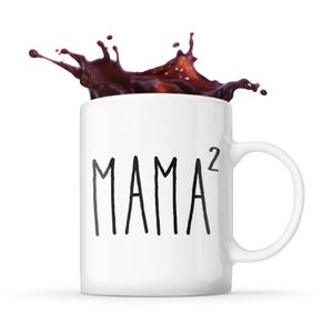 Può includere: Tazza da caffè in ceramica bianca con una scritta nera che dice "MAMA^2". Il caffè schizza fuori dalla tazza.