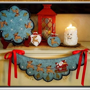 May include: A blue felt Christmas garland with a Santa Claus and reindeer design. The garland is decorated with white snowflakes and green trees. It is hanging on a white mantel with a red ribbon.