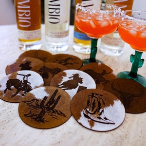 Peut inclure: Une composition de bouteilles de tequila, de verres &agrave; margarita et de dessous de verre d&eacute;coratifs. Les dessous de verre pr&eacute;sentent des motifs sur le th&egrave;me de l'Ouest, notamment des cow-boys, des cactus et des bottes. Les bouteilles de tequila portent le mot "CAMBIO".
