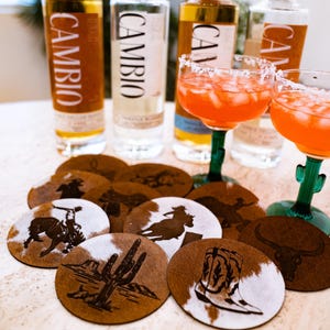 Peut inclure: Nature morte avec des bouteilles de tequila, des cocktails et des dessous de verre. Les bouteilles de tequila portent l'inscription "CAMBIO". Les dessous de verre ont un motif en peau de vache et des motifs sur le th&egrave;me de l'Ouest.