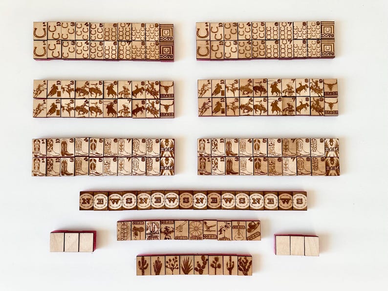 May include: Wooden game tiles with engraved Western-themed designs, including horseshoes, cowboys, boots, and cacti. The tiles are arranged in rows and columns, with some featuring the word "NEWS". The tiles are light brown with dark brown engravings.