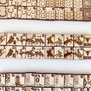 May include: Wooden game tiles with etched designs. The tiles feature images of horseshoes, cowboys, cowboy boots, and cowboys riding horses. The tiles are arranged in rows and columns, with numbers and symbols.