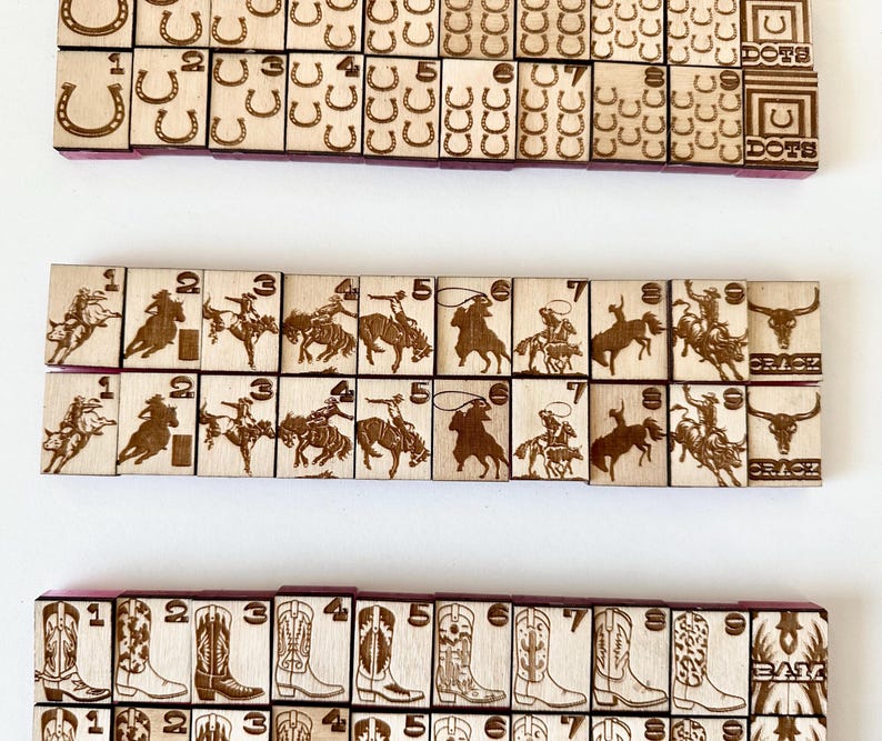 May include: Wooden game tiles with etched designs. The tiles feature images of horseshoes, cowboys, cowboy boots, and cowboys riding horses. The tiles are arranged in rows and columns, with numbers and symbols.