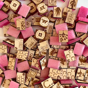 May include: A collection of wooden and pink resin game pieces. The wooden pieces feature etched designs of cacti, horseshoes, and cowboy boots. The pink resin pieces are rectangular and scattered among the wooden pieces.