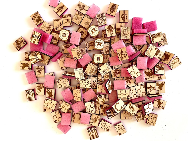 May include: A collection of small, wooden tiles with etched designs and pink, rectangular blocks. The wooden tiles feature various illustrations, including horseshoes, cacti, and other symbols. The pink blocks are scattered among the wooden tiles.