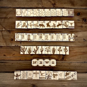 May include: Wooden tiles with engraved Western-themed images, including horseshoes, cowboys, boots, cacti, and the word "NEWS." The tiles are arranged on a wooden surface, creating a rustic aesthetic. The word "DOTE" is also visible.