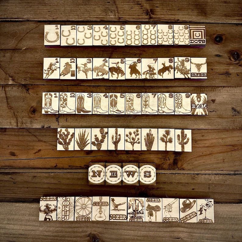 May include: Wooden tiles with engraved Western-themed images, including horseshoes, cowboys, boots, cacti, and the word "NEWS." The tiles are arranged on a wooden surface, creating a rustic aesthetic. The word "DOTE" is also visible.