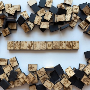 May include: Wooden tiles with engraved Western-themed designs, including boots, horseshoes, and cacti. Some tiles are black, others are natural wood. The tiles are arranged in a scattered pattern, with a line of tiles in the center.
