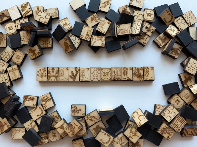 May include: Wooden tiles with engraved Western-themed designs, including boots, horseshoes, and cacti. Some tiles are black, others are natural wood. The tiles are arranged in a scattered pattern, with a line of tiles in the center.
