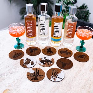 Peut inclure: Bouteilles de tequila avec le mot "CAMBIO" sur l'&eacute;tiquette, accompagn&eacute;es de cocktails dans des verres &agrave; pied verts. Des dessous de verre ronds avec des motifs de cow-boy sont dispos&eacute;s devant les bouteilles.