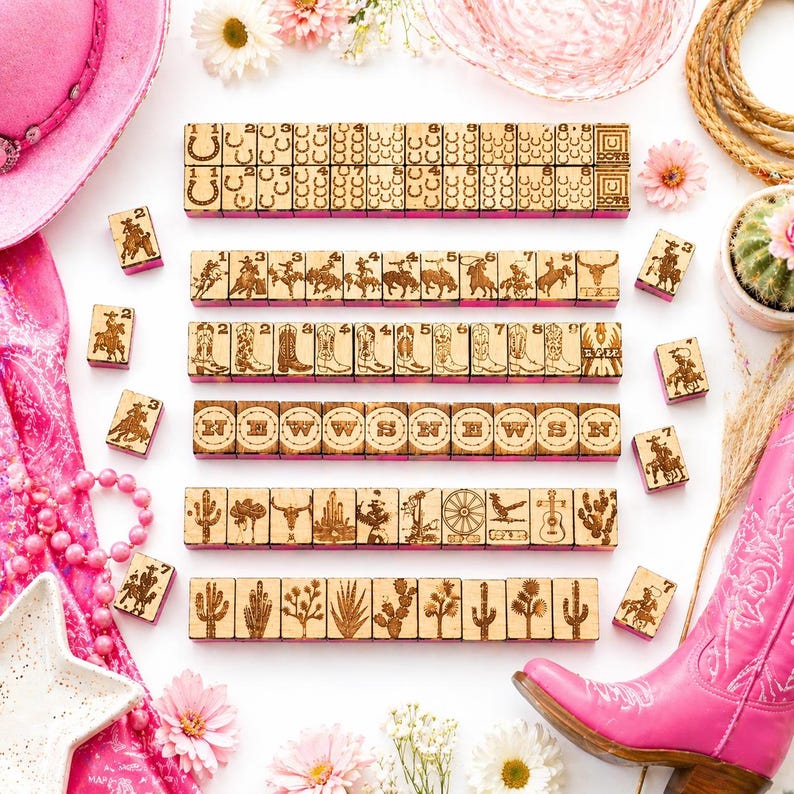 May include: Wooden game pieces with cowboy-themed designs, including horseshoes, cowboys, boots, and cacti. The pieces are arranged with a pink cowboy hat and boot, flowers, and a rope. The game pieces are made of wood.
