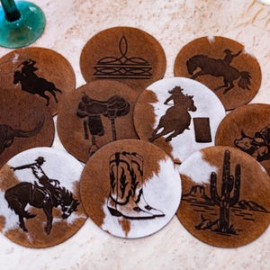 Peut inclure: Ensemble de dessous de verre ronds avec un motif de peau de vache marron et blanc. Chaque dessous de verre pr&eacute;sente un motif grav&eacute; diff&eacute;rent, comme un cow-boy &agrave; cheval, un cr&acirc;ne de taureau, une selle et un cactus. Th&egrave;me western.