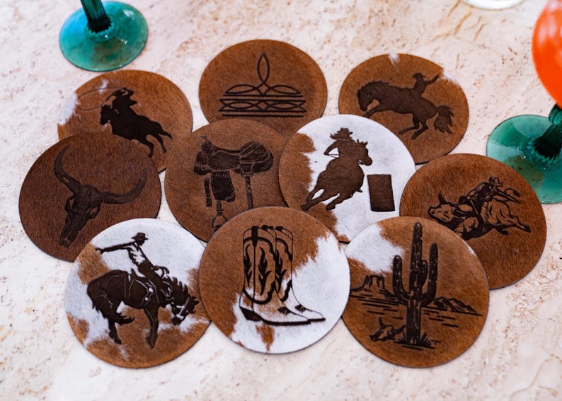 Peut inclure: Ensemble de dessous de verre ronds avec un motif de peau de vache marron et blanc. Chaque dessous de verre pr&eacute;sente un motif grav&eacute; diff&eacute;rent, comme un cow-boy &agrave; cheval, un cr&acirc;ne de taureau, une selle et un cactus. Th&egrave;me western.