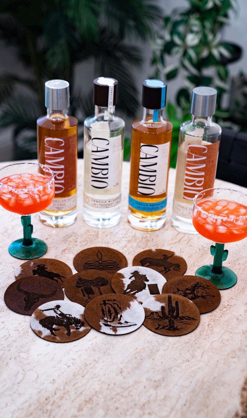 Peut inclure: Quatre bouteilles de tequila Cambio avec diff&eacute;rentes &eacute;tiquettes et un cocktail margarita dans un verre vert en forme de cactus. Plusieurs dessous de verre ronds avec des motifs sur le th&egrave;me de l'Ouest sont &eacute;galement visibles.