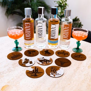Peut inclure: Pr&eacute;sentation de bouteilles de tequila et de cocktails dans des verres bord&eacute;s de sel. Les bouteilles portent l'inscription "CAMBIO". Des dessous de verre sur le th&egrave;me des cow-boys sont &eacute;galement pr&eacute;sents. Les cocktails sont servis dans des verres verts en forme de cactus.