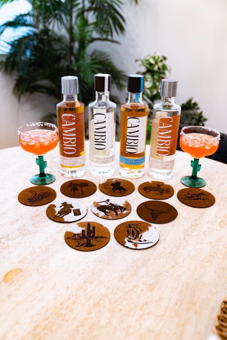 Peut inclure: Pr&eacute;sentation de bouteilles de tequila et de cocktails dans des verres bord&eacute;s de sel. Les bouteilles portent l'inscription "CAMBIO". Des dessous de verre sur le th&egrave;me des cow-boys sont &eacute;galement pr&eacute;sents. Les cocktails sont servis dans des verres verts en forme de cactus.