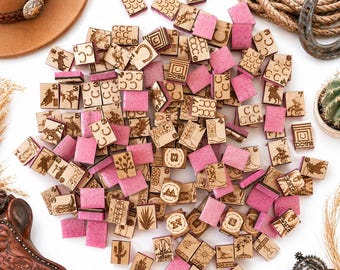 May include: A collection of small, wooden, and pink square tiles with various Western-themed designs, including cowboys, horseshoes, and cacti. Some tiles have the word "DORE" etched on them. A brown cowboy hat, rope, and horseshoe are also visible.