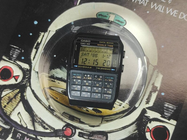 May include: A black Casio DBC-62 Data Bank watch with a digital display showing the date, time, and day of the week. The watch also has a calculator function and a world time function.