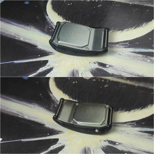 May include: The back of a black digital watch with a silver metal case. The watch has a silver metal band and a black button on the side.