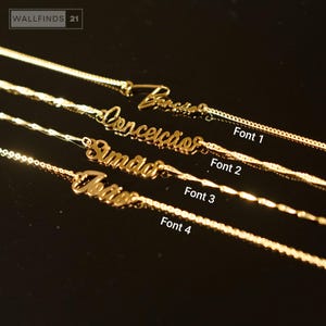 Op de afbeelding: Gouden naamkettingen in vier verschillende lettertypen. Elke ketting heeft een naam in een cursieve of blokletterstijl. De kettingen worden getoond op een donkere ondergrond, met de tekst "Font 1", "Font 2", "Font 3" en "Font 4" zichtbaar.