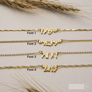 May include: Four gold-toned necklaces featuring custom nameplates in Amharic script, each displayed with a different chain style and labeled Font 1, Font 2, Font 3, and Font 4. The necklaces are arranged horizontally, showcasing distinct metal link designs.