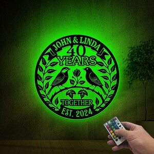 May include: A black metal sign with a green glow, celebrating 40 years together. The sign features two birds perched on a branch with leaves, a rose, and the text "John & Linda 40 Years Together Est. 2024".
